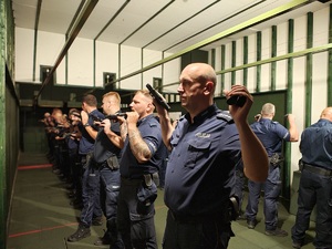 Policjanci stoją w rzędzie, pokazują broń do przejrzenia.