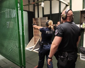 Policjantka mierzy pistoletem do celu, za nią stoją instruktorzy.
