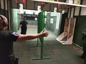 Policjant biegnie w stronę robiącego zdjęcie, a instruktor pokazuje ręką, gdzie należy skręcić w stronę miejsca strzelania.