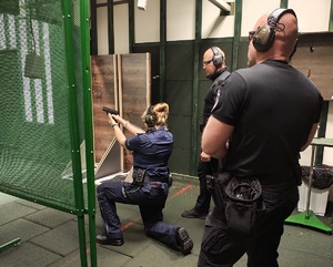 Policjant klęczy, strzela do celu. Za nim stoją instruktorzy.
