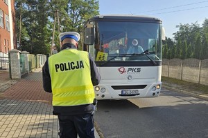 Policjant jest odwrócony tyłem, idzie w kierunku zaparkowanego autobusu.
