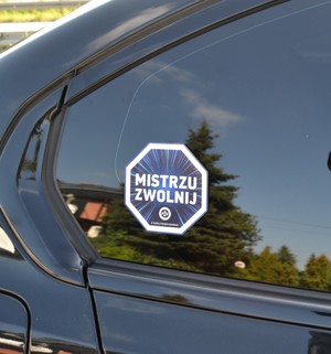 Na szybie samochodu przyklejona jest naklejka &quot;Mistrzu zwolnij&quot;.
