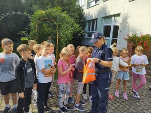 Policjantka rozdaje dzieciom odblaski przed budynkiem szkoły.