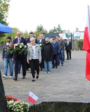 W kolejce czekają osoby z kwiatami, by je złożyć pod pomnikiem.