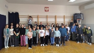 Sala gimnastyczna. Policjant pozuje ze starszymi uczniami do grupowego zdjęcia.