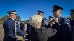 Policjanci stoją w szeregu, jednemu z nich kobieta wpina medal do munduru.