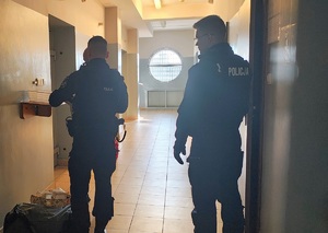Pomieszczenie PDOZ w komendzie. Policjanci sprawdzają osobę zatrzymaną. Przygotowują do konwoju.