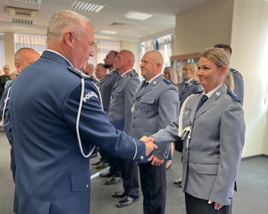 W dwuszeregu stoją mianowani policjanci, komendant podaje rękę policjantce. Gratuluje jej.