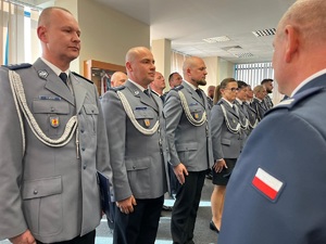 W dwuszeregu stoją mianowani policjanci, komendant podaje im rękę i akty mianowania, gratuluje im.