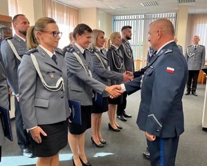 W dwuszeregu stoją mianowani policjanci, komendant podaje im rękę i akty mianowania, gratuluje im.