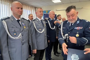 Policjanci stoją w dwuszeregu. Podchodzi do nich przewodniczący i wpina w klapy marynarek medal.