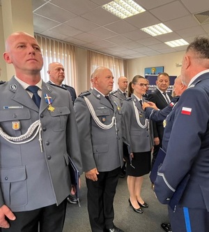 Policjanci stoją w dwuszeregu. Podchodzi do nich przewodniczący i wpina w klapy marynarek medal.