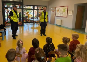 Policjanci stoją przed dziećmi. Mają założone kamizelki odblaskowe.
