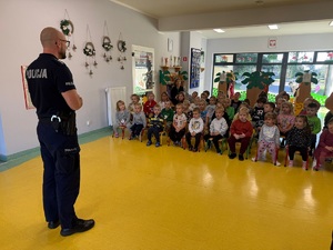 Policjant mówi do dzieci, które siedzą na krzesełkach na wprost.