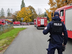 Policjant stoi przy wozie strażackim tyłem do zdjęcia.