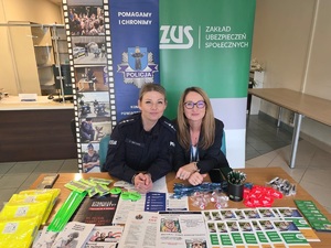 Policjantka umundurowana w towarzystwie pracownika zus przy stoisku profilaktyczno - informacyjnym.