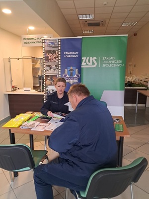 Rozmowa policjantki z seniorem przy stoisku profilaktyczno - informacyjnym o sposobach działania oszustów.