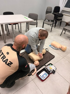 Mieszkaniec wykonujący resuscytację krążeniowo-oddechową pod nadzorem strażaka z Ochotniczej Straży Pożarnej.