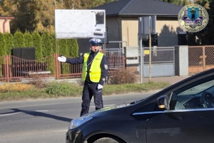 Policjant na drodze kieruje ruchem. ma założony mundur i kamizelkę odblaskową.