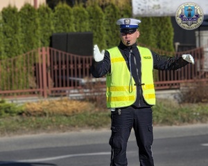 Policjant na drodze kieruje ruchem. ma założony mundur i kamizelkę odblaskową.