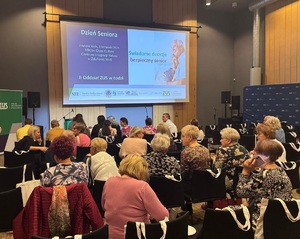 Sala, na krzesełkach, tyłem do zdjęcia siedzi publiczność. Na wprost nich na ścianie jest rzutnik, wyświetlana jest prezentacja.