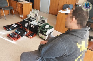 Po prawej stronie, na krzesełku siedzi zatrzymany. Przed nim na podłodze leżą elektronarzędzia.