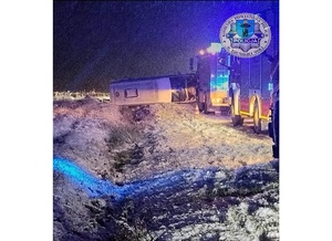 Noc, w rowie na boku leży przewrócony bus. Obok wzdłuż drogi stoją pojazdy służb ratunkowych.