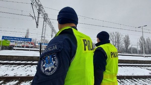 Dwóch umundurowanych policjantów patrzy na tory, w tle napis Zduńska Wola Karsznice.