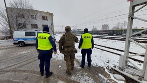 Dwóch policjantów i żołnierz idą wzdłuż torów.