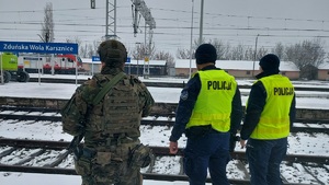 Policjanci i żołnierz patrzą na tory, stoją w pobliżu torowiska, w tle napis Zduńska Wola Karsznice.