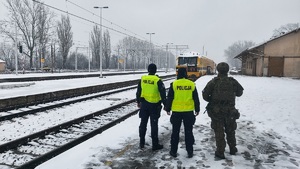 Policjanci i żołnierz idą w stronę pociągu, który nadjeżdża w ich kierunku.