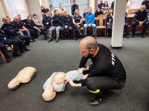 Aula w komendzie. Strażak pokazuje fantoma niemowlaka.