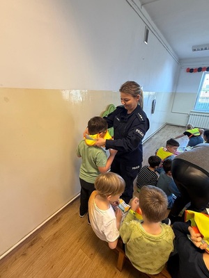 Umundurowana policjantka pomagająca założyć dziecku kamizelkę odblaskową.