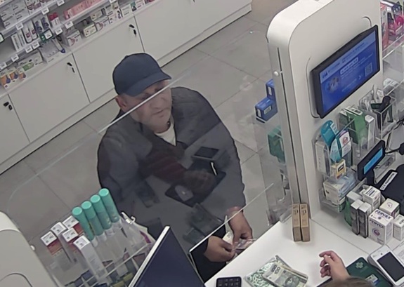 Przy kasie w aptece stoi mężczyzna. Trzyma w rękach pieniądze.