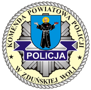 Okrągłe logo. W środku napis Komenda Powiatowa Policji w Zduńskiej Woli. W środku postać św. M.M Kolbe. Napis Policja na policyjnej odznace.
