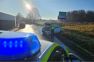 Radiowóz, po prawej stronie policjantka obok rozbitego samochodu pisze dokumentację. Dalej znak drogowy miejscowości Czechy.