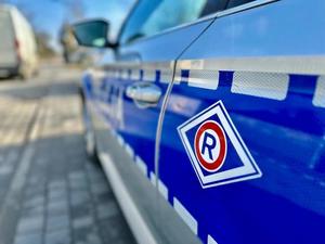 Bok oznakowanego radiowozu, widoczne logo ruchu drogowego - litera R, naklejona na drzwiach radiowozu.