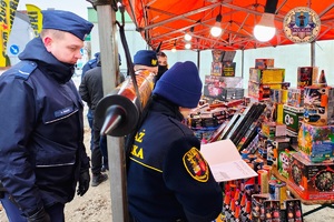 Policjant oraz strażnicy miejscy oglądają dokumentację sprzedawcy dotyczącą sprzedaży fajerwerków.