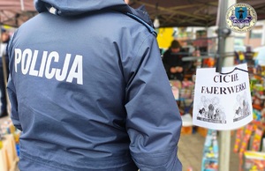 Stojący tyłem do zdjęcia policjant ogląda fajerwerki. Obok wisi kartka z napisem ciche fajerwerki.