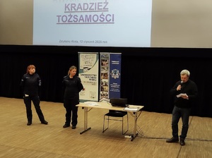 Na scenie stoją dwie policjantki i mężczyzna, Za nimi na ekranie wyświetla się napis: kradzież tożsamości.