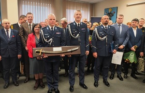 Inspektor Robert Krawczyk z szablą, pozuje na tle zebranych gości do zdjęcia z szablą.