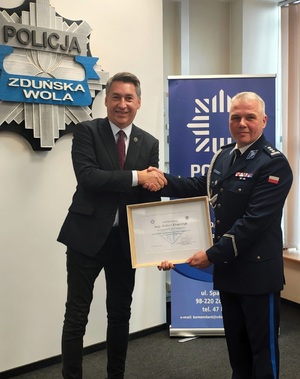 Mężczyzna wręcza komendantowi wydrukowane podziękowania w ramce. Pozują razem do zdjęcia.