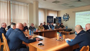 Aula komendy. Za stołami siedzą policjanci i goście odprawy. Na ścianie z projektora wyświetlana jest prezentacja podsumowująca miniony rok.