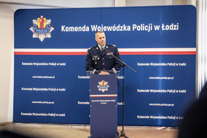 Komendant wojewódzki przemawia do zebranych, stoi za mównicą. Za nim w tle napis Komenda Wojewódzka Policji w Łodzi.