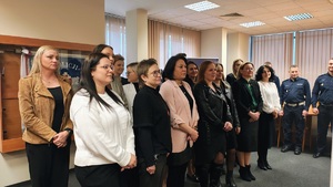 W auli, pod ścianą stoją pracownicy cywilni. W tle widać stojących policjantów w mundurach.