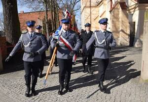 Poczet sztandarowy policjantów maszeruje w stronę pomnika. Za tym pocztem widać kolejne idące za nim.