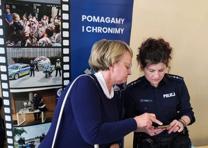 Kobieta pokazuje policjantce swój telefon, na którym coś pokazuje.