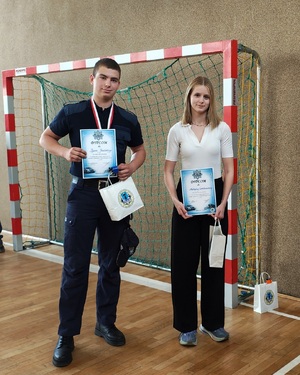 Chłopak z dziewczyną trzymają dyplomy i nagrody, pozują razem do zdjęcia.