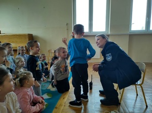 Policjantka siedzi na krzesełku, przed nią stoi chłopczyk tyłem do zdjęcia.