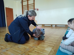 Policjantka kuca na podłodze, przed nią leży dziecko w bezpiecznej pozycji "na żółwia".